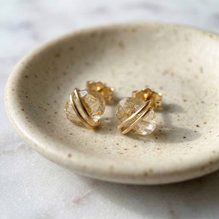 Gold rutilated quartz gold filled wire wrapped stud earrings minimalist and simple minimalist and unique crystal studs bisected ovals with center accent on ceramic jewelry dish