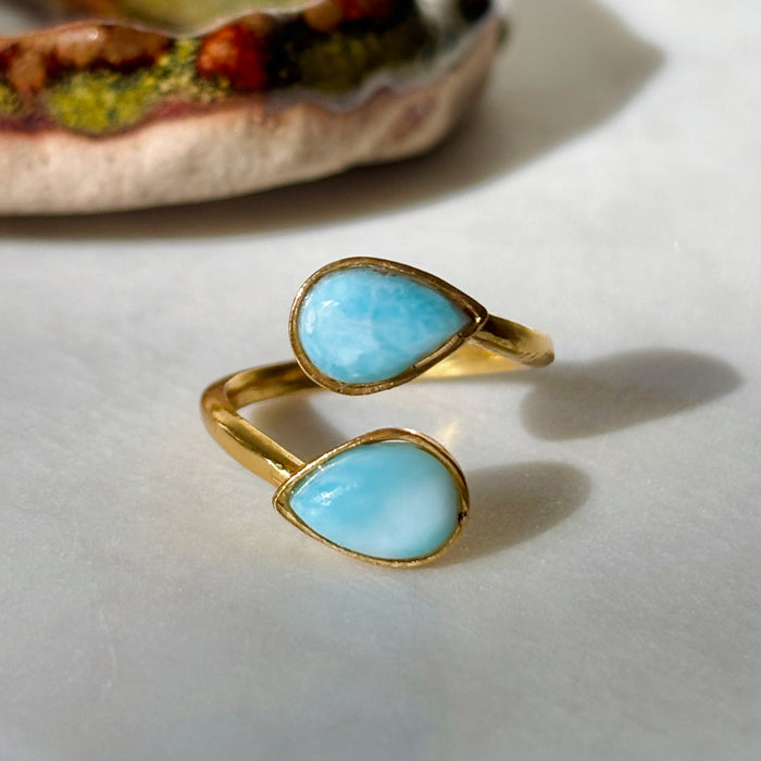 Gold larimar adjustable teardrop two stone ring in front of ceramic dish